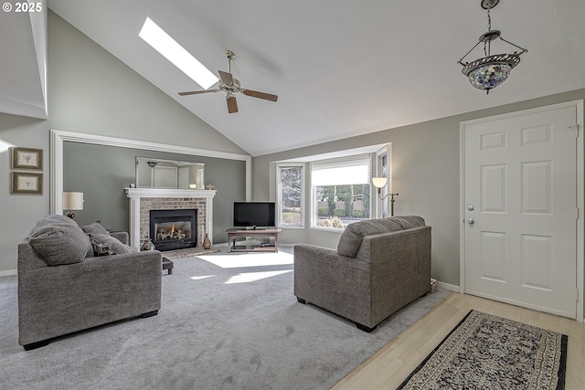 living room with ceiling fan, a skylight, high vaulted ceiling, a fireplace, and light hardwood / wood-style floors