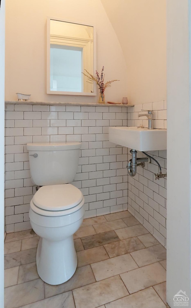 bathroom featuring toilet, tile walls, and sink