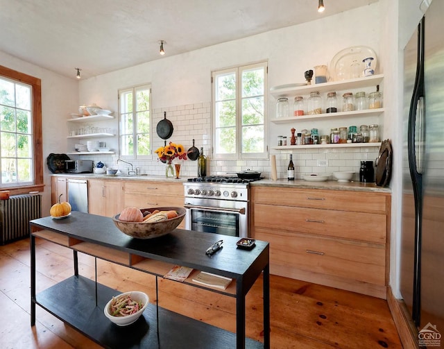 kitchen with backsplash, radiator, a wealth of natural light, and appliances with stainless steel finishes