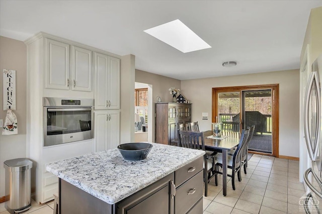 kitchen with stainless steel appliances, light tile patterned flooring, a kitchen island, baseboards, and a skylight