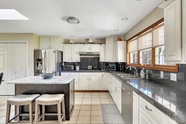 kitchen featuring light tile patterned floors, decorative backsplash, a sink, appliances with stainless steel finishes, and under cabinet range hood