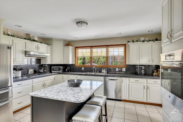 kitchen featuring light tile patterned floors, tasteful backsplash, a sink, appliances with stainless steel finishes, and under cabinet range hood