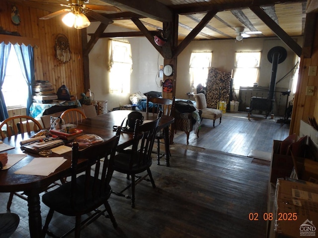 dining room featuring wood walls, vaulted ceiling with beams, a wood stove, dark hardwood / wood-style floors, and ceiling fan