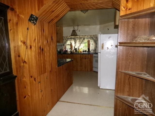 kitchen featuring white fridge, stove, and wood walls