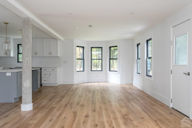 unfurnished living room featuring decorative columns and light hardwood / wood-style floors