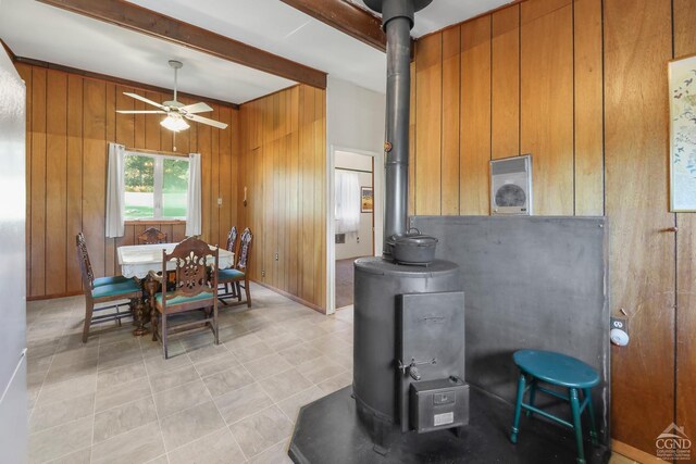 kitchen with beam ceiling, a wood stove, wood walls, and ceiling fan