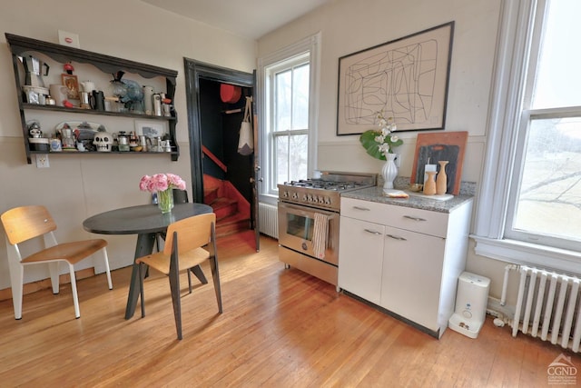 kitchen featuring stainless steel range, light wood-type flooring, white cabinetry, and radiator