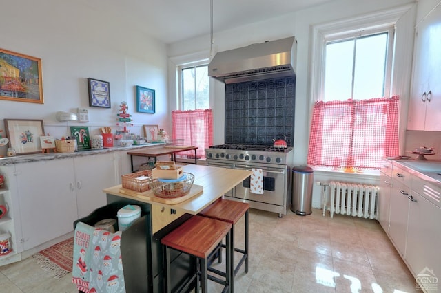 kitchen featuring radiator, white cabinetry, wall chimney exhaust hood, and high end stainless steel range oven