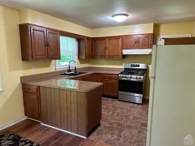 kitchen with stainless steel gas range oven, sink, white fridge, dark hardwood / wood-style flooring, and kitchen peninsula