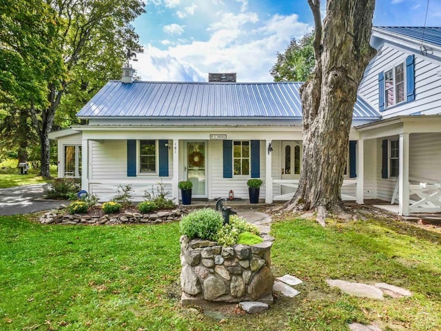 view of front facade featuring metal roof, a front yard, covered porch, and a chimney