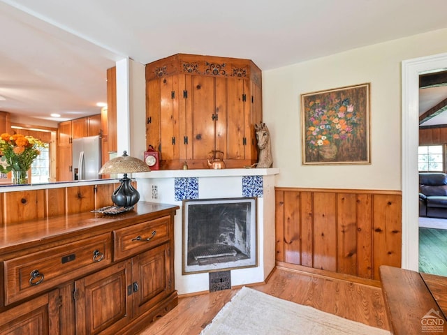 kitchen featuring wainscoting, brown cabinets, light wood-type flooring, and stainless steel fridge with ice dispenser