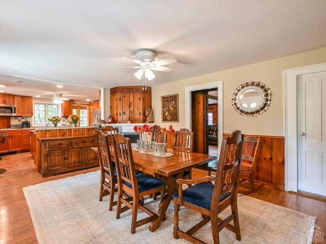 dining room featuring a ceiling fan, a wainscoted wall, and light wood finished floors