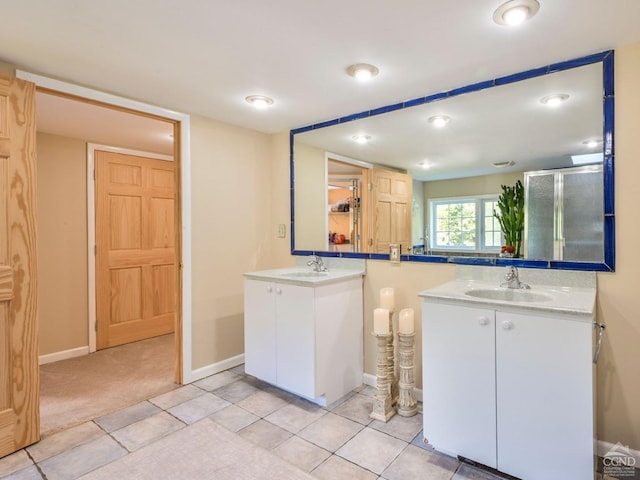 full bath featuring a stall shower, two vanities, baseboards, and a sink