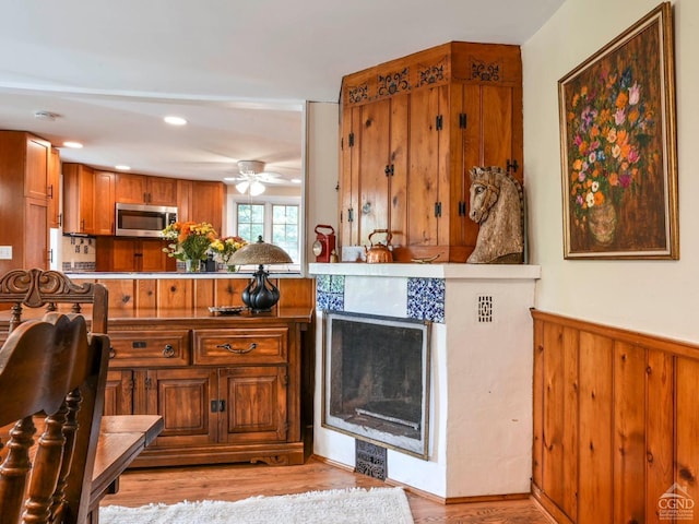 kitchen featuring a ceiling fan, a wainscoted wall, light wood finished floors, stainless steel microwave, and brown cabinets