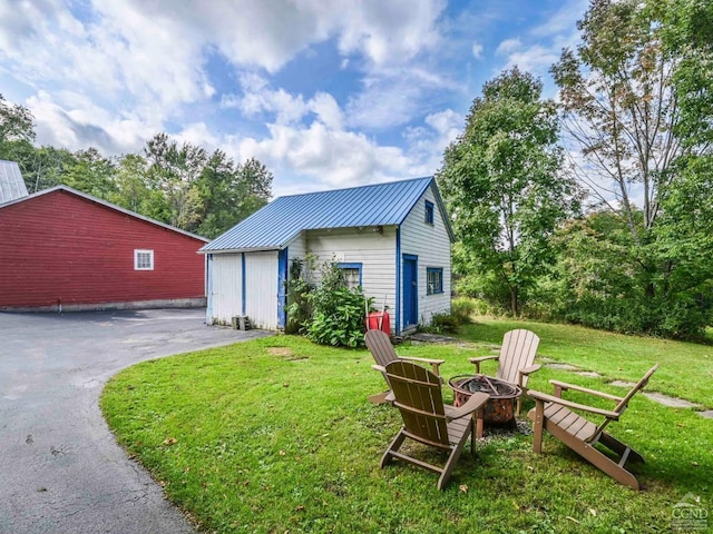 exterior space featuring an outbuilding, driveway, an outdoor fire pit, a yard, and metal roof