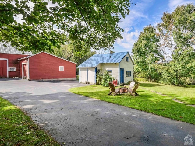 view of front of property with an outdoor fire pit, a front yard, metal roof, a garage, and an outbuilding