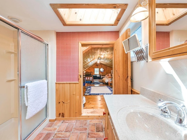 full bath featuring stone finish flooring, vanity, wood walls, and a shower stall