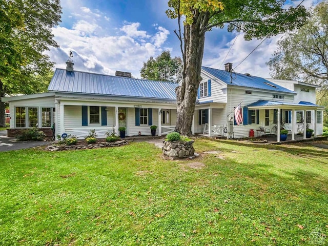 back of house featuring metal roof, a yard, a porch, and a chimney