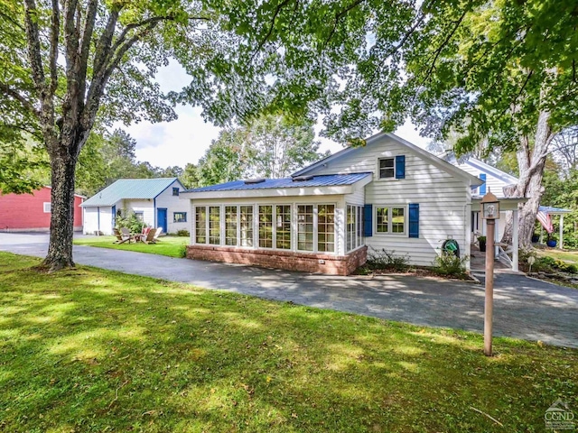 view of front of home with brick siding, aphalt driveway, a front yard, metal roof, and a sunroom