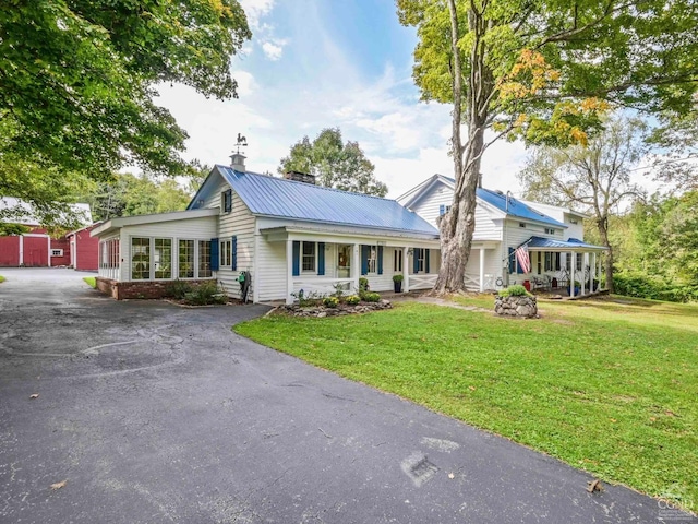 view of front of house with a front yard, covered porch, driveway, and metal roof