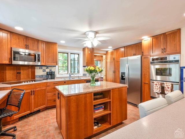 kitchen featuring brown cabinets, a sink, a center island, stainless steel appliances, and light stone countertops