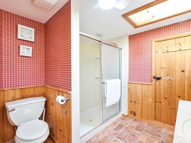 full bath featuring a shower stall, wallpapered walls, toilet, wainscoting, and a skylight