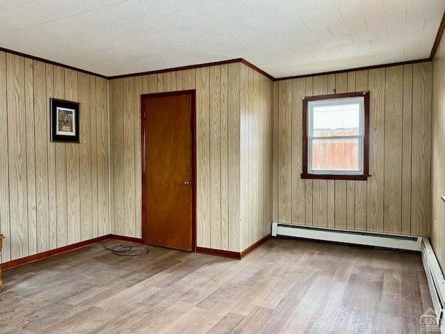 empty room featuring a baseboard heating unit, crown molding, light wood-type flooring, and baseboards