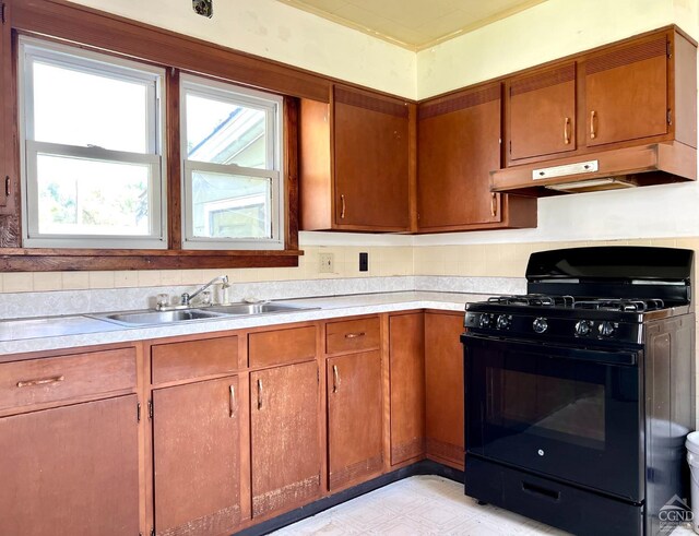 kitchen featuring brown cabinets, light countertops, black gas stove, a sink, and under cabinet range hood