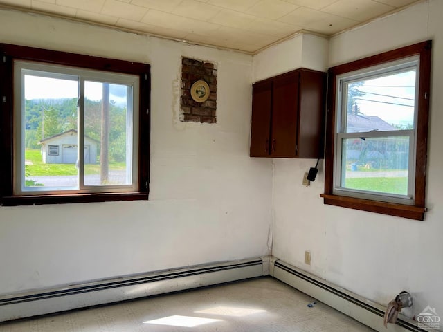 empty room featuring a baseboard heating unit, a healthy amount of sunlight, and light floors