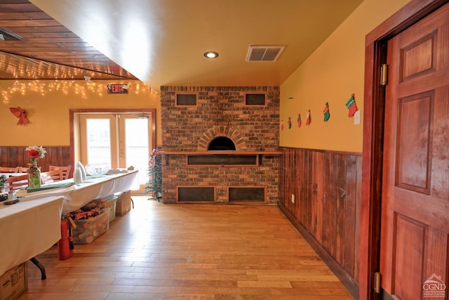 living room featuring lofted ceiling, french doors, wooden walls, light hardwood / wood-style flooring, and a fireplace