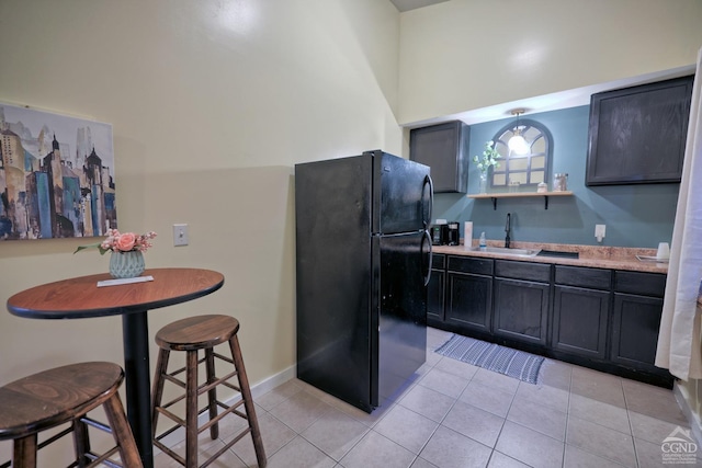 kitchen with light tile patterned floors, black fridge, and sink