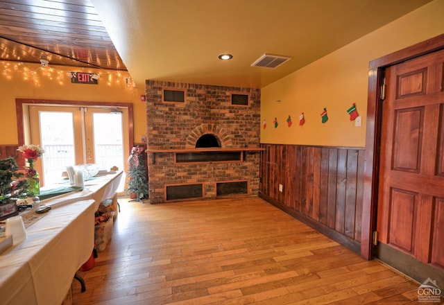 living room featuring a fireplace, wood walls, light hardwood / wood-style flooring, and french doors