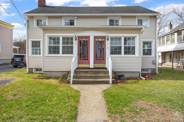 view of front facade featuring entry steps, a front yard, roof with shingles, and a chimney