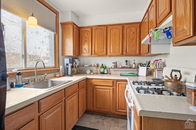 kitchen featuring brown cabinetry, under cabinet range hood, a sink, and gas range gas stove