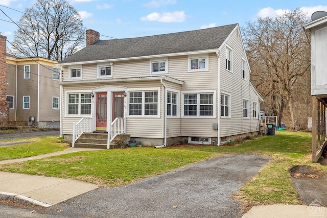 view of front of home featuring roof with shingles, a chimney, and a front lawn