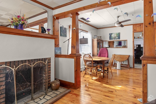 living area featuring light wood finished floors, a fireplace with raised hearth, a ceiling fan, and crown molding
