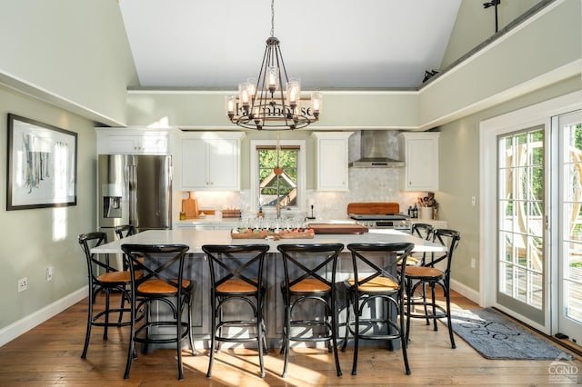 kitchen with white cabinets, wall chimney range hood, light wood-type flooring, a notable chandelier, and a kitchen bar