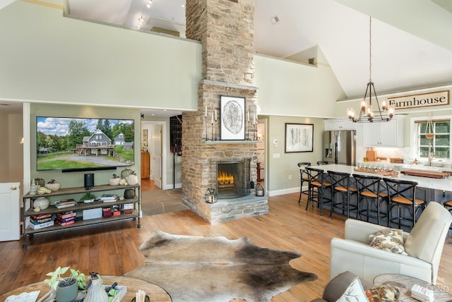 living room featuring a stone fireplace, light hardwood / wood-style flooring, high vaulted ceiling, and a notable chandelier