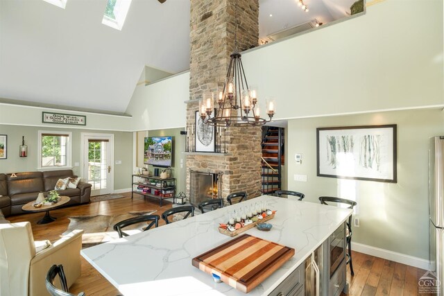 kitchen with high vaulted ceiling, a stone fireplace, hanging light fixtures, a skylight, and wood-type flooring