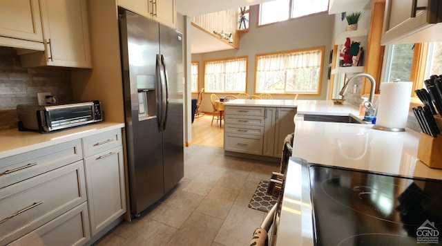 kitchen featuring a toaster, light tile patterned floors, backsplash, a sink, and stainless steel refrigerator with ice dispenser