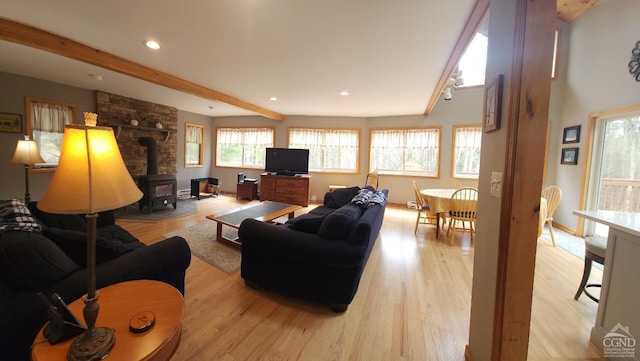 living room featuring beam ceiling, a healthy amount of sunlight, light wood-style flooring, and a wood stove