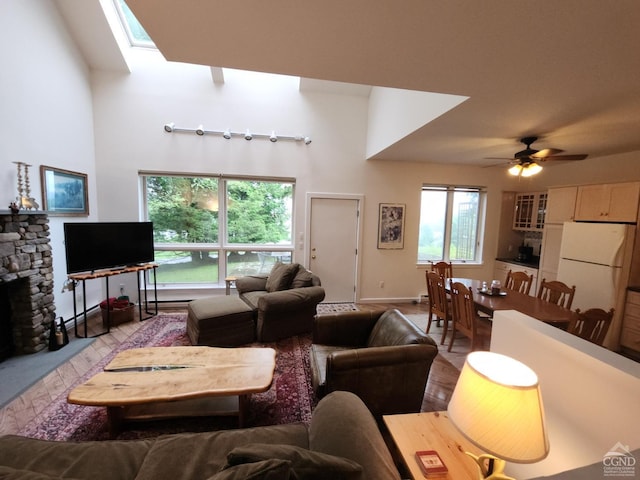 living room with a stone fireplace, a wealth of natural light, and ceiling fan