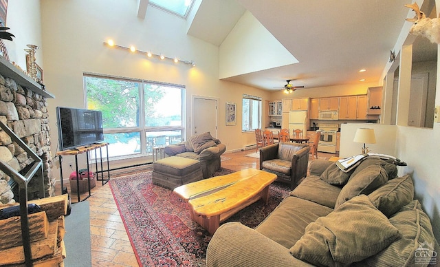 living room with a skylight, ceiling fan, a stone fireplace, and a high ceiling