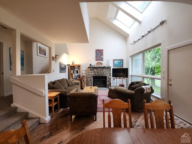 living room with a stone fireplace, wood-type flooring, high vaulted ceiling, and a skylight