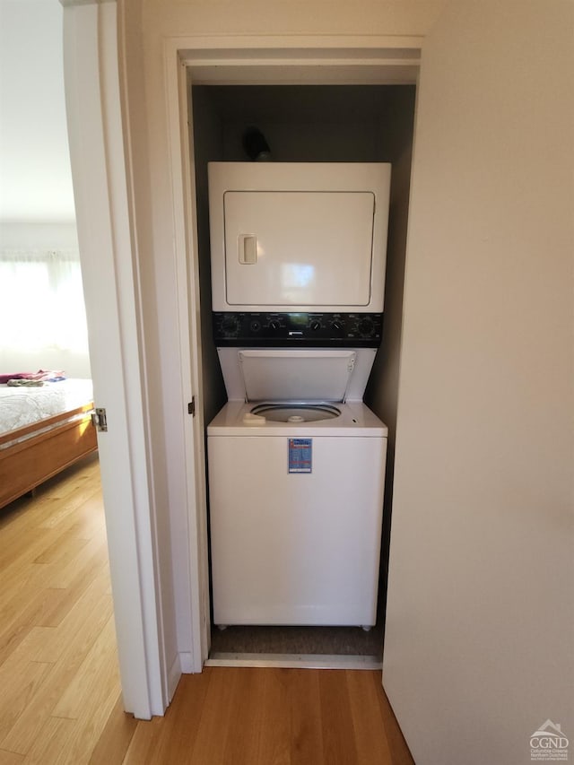 clothes washing area with stacked washer and clothes dryer and light wood-type flooring