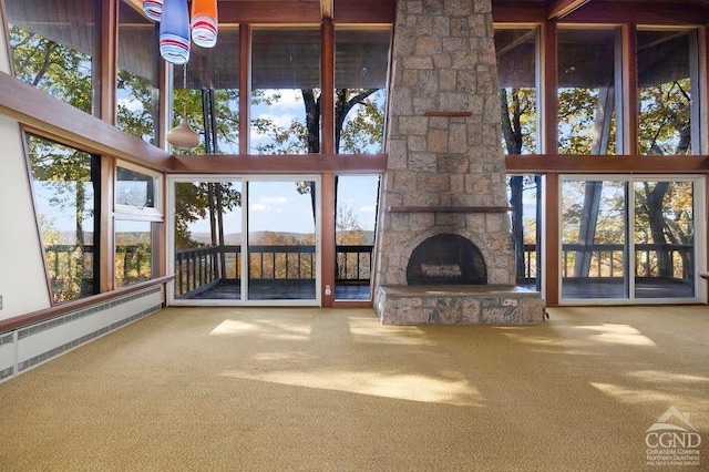 unfurnished living room featuring carpet, a towering ceiling, a baseboard radiator, and a stone fireplace