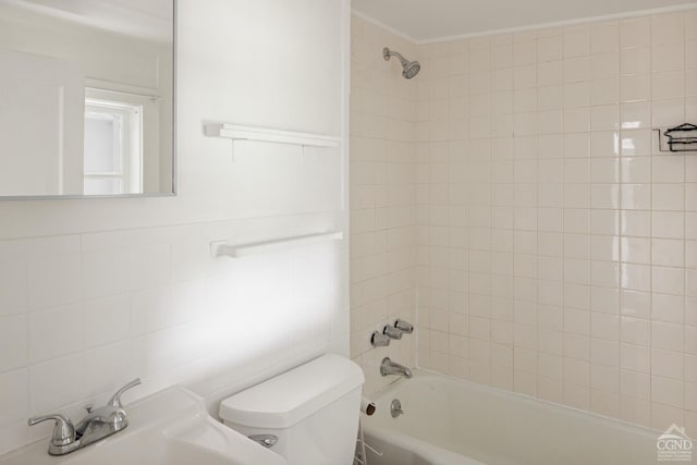 bathroom featuring toilet, tiled shower / bath, and tile walls