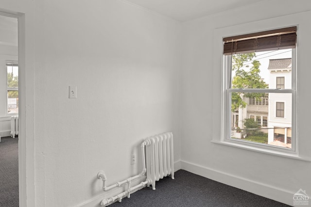 empty room featuring dark colored carpet, radiator heating unit, and a wealth of natural light