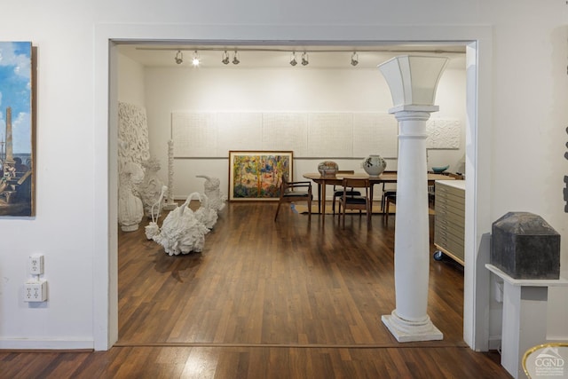 hallway featuring decorative columns, dark hardwood / wood-style flooring, and rail lighting