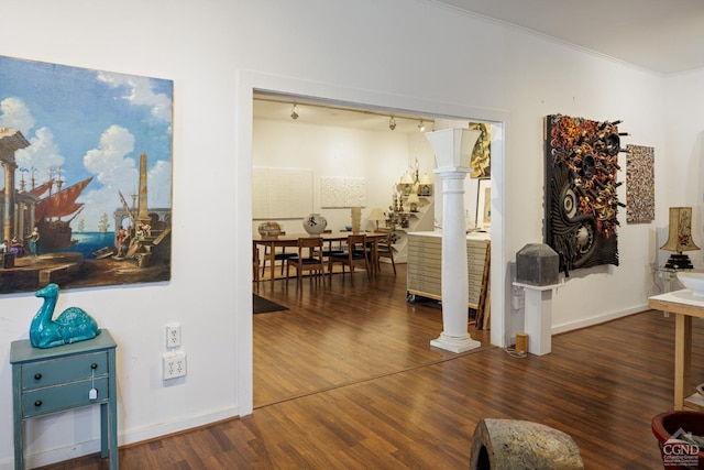 corridor featuring ornate columns, track lighting, dark hardwood / wood-style floors, and ornamental molding